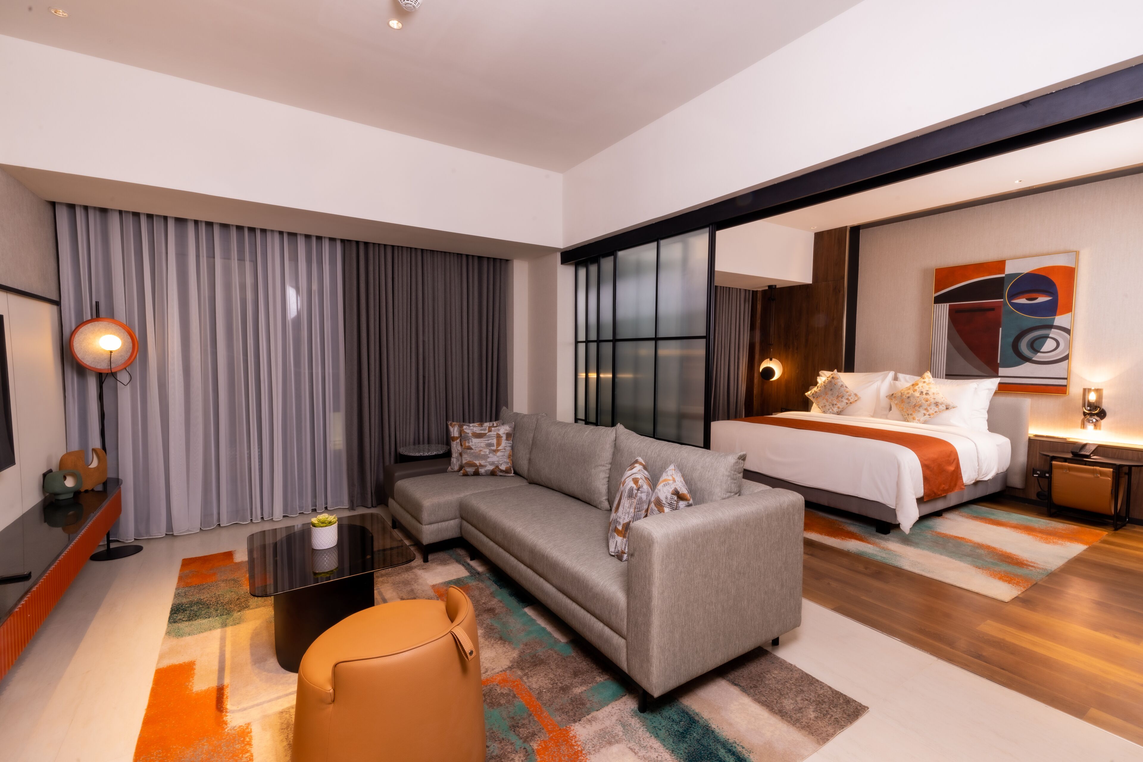 A modern hotel room with a sofa, a bed, a desk, and a large window.