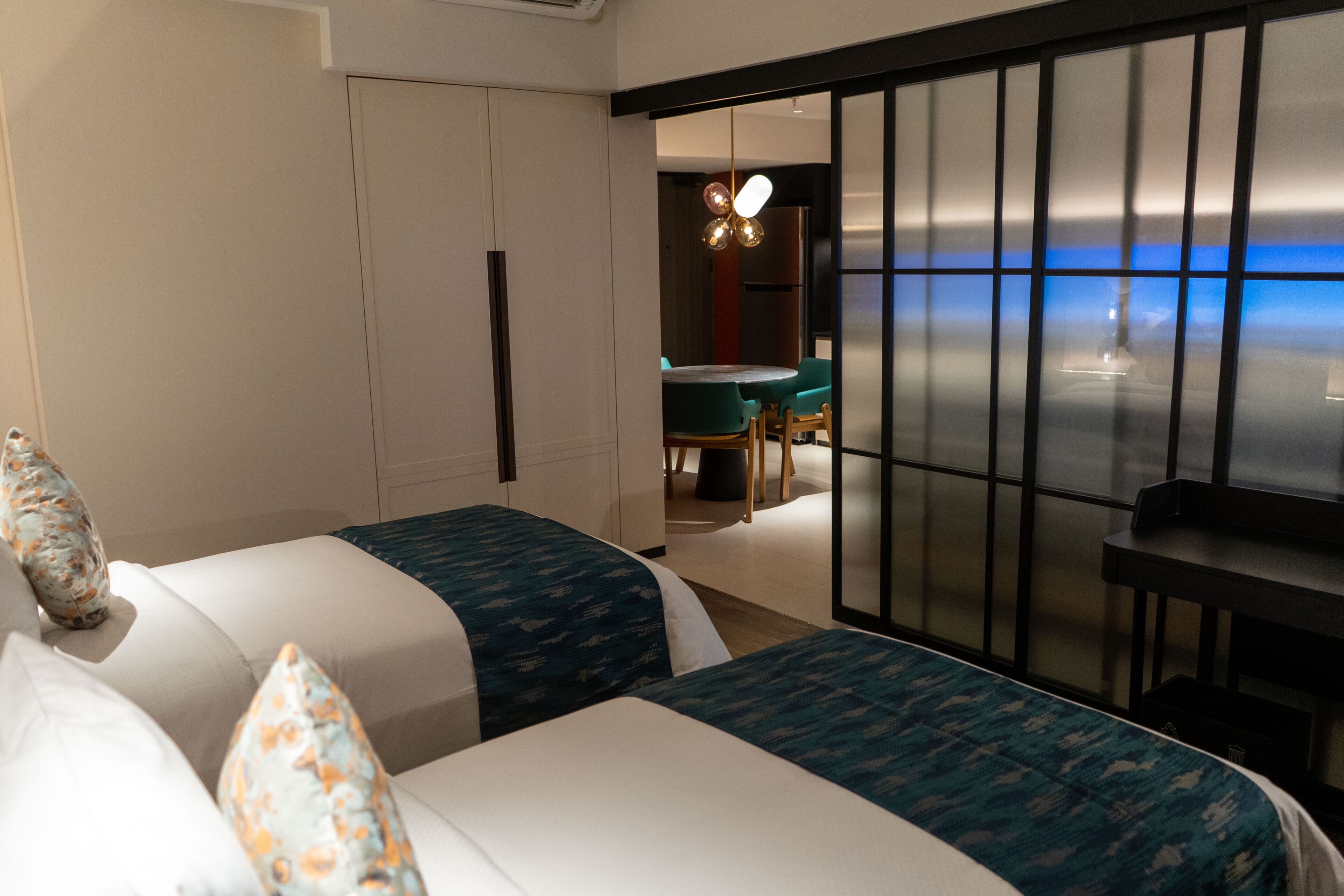 A hotel room with two beds, a desk, and a view of the sea.