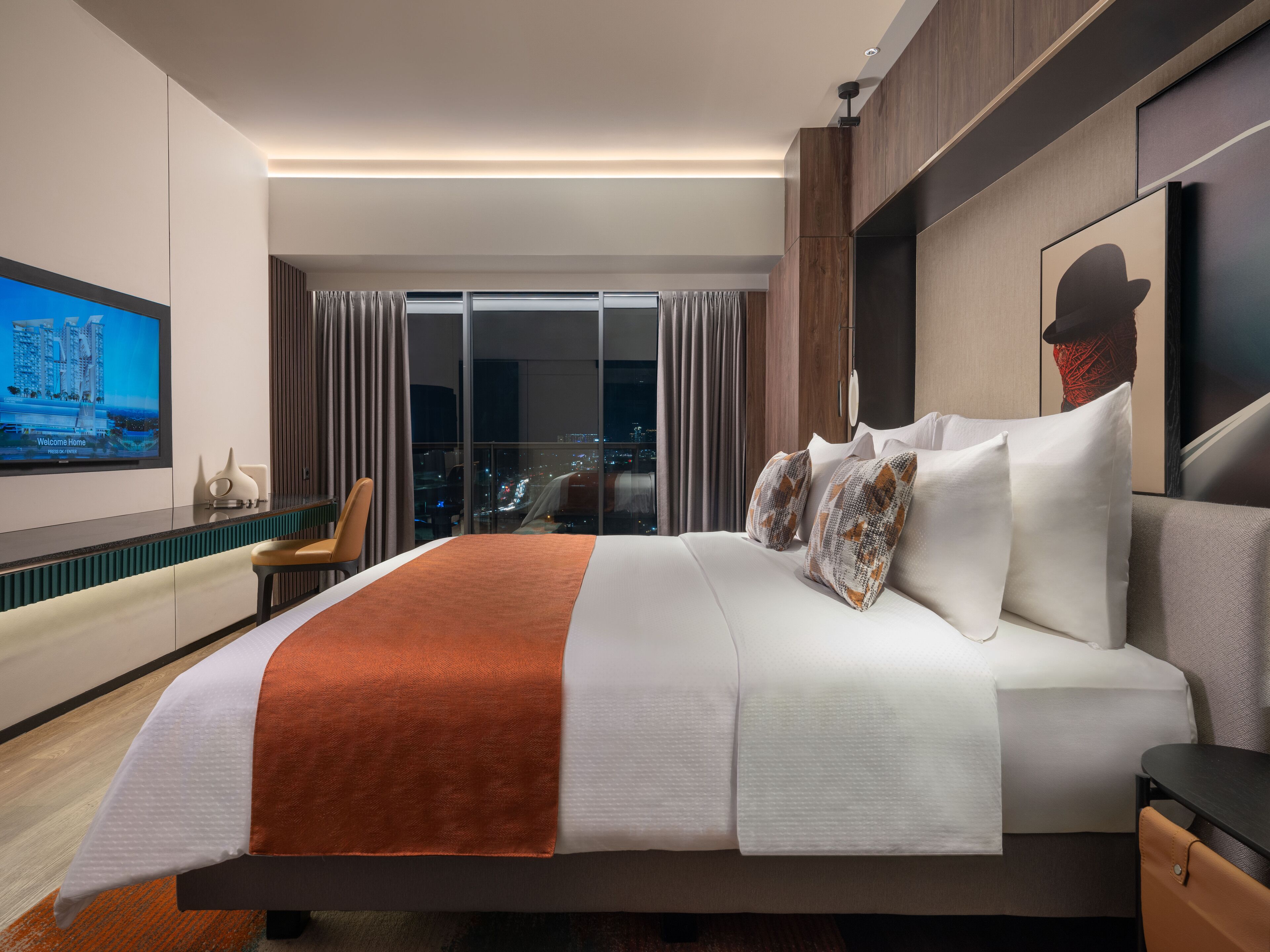 A modern hotel room with a large bed, a city view, and a flat-screen TV on the wall.