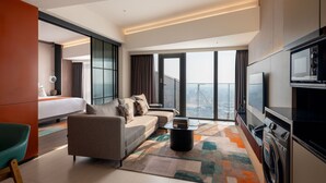 A modern hotel room with a large bed, a sofa, a TV, and a washing machine. - Herloom BSD (Gading Serpong)