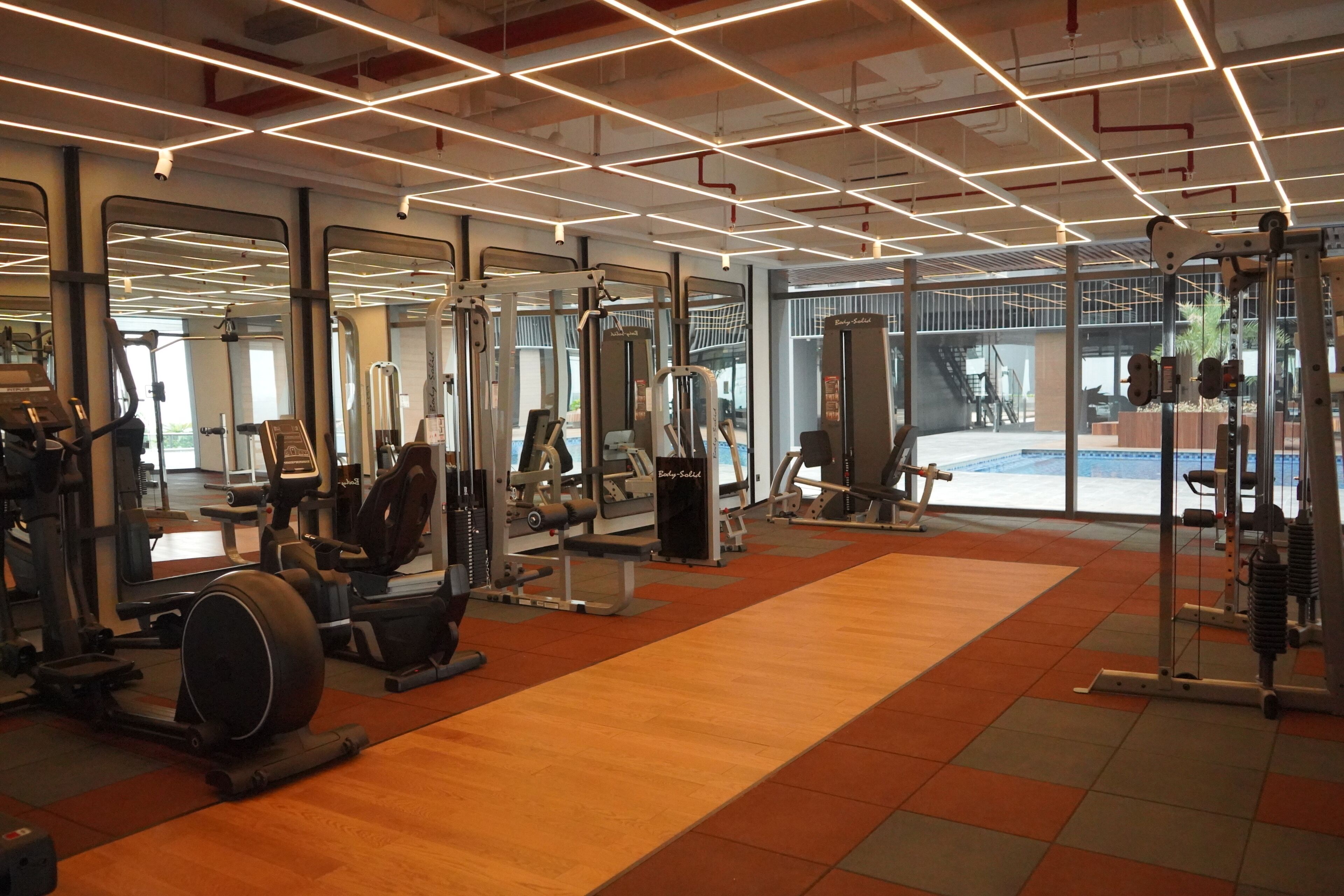 A gym with various exercise equipment, large mirrors, and a view of an outdoor area.