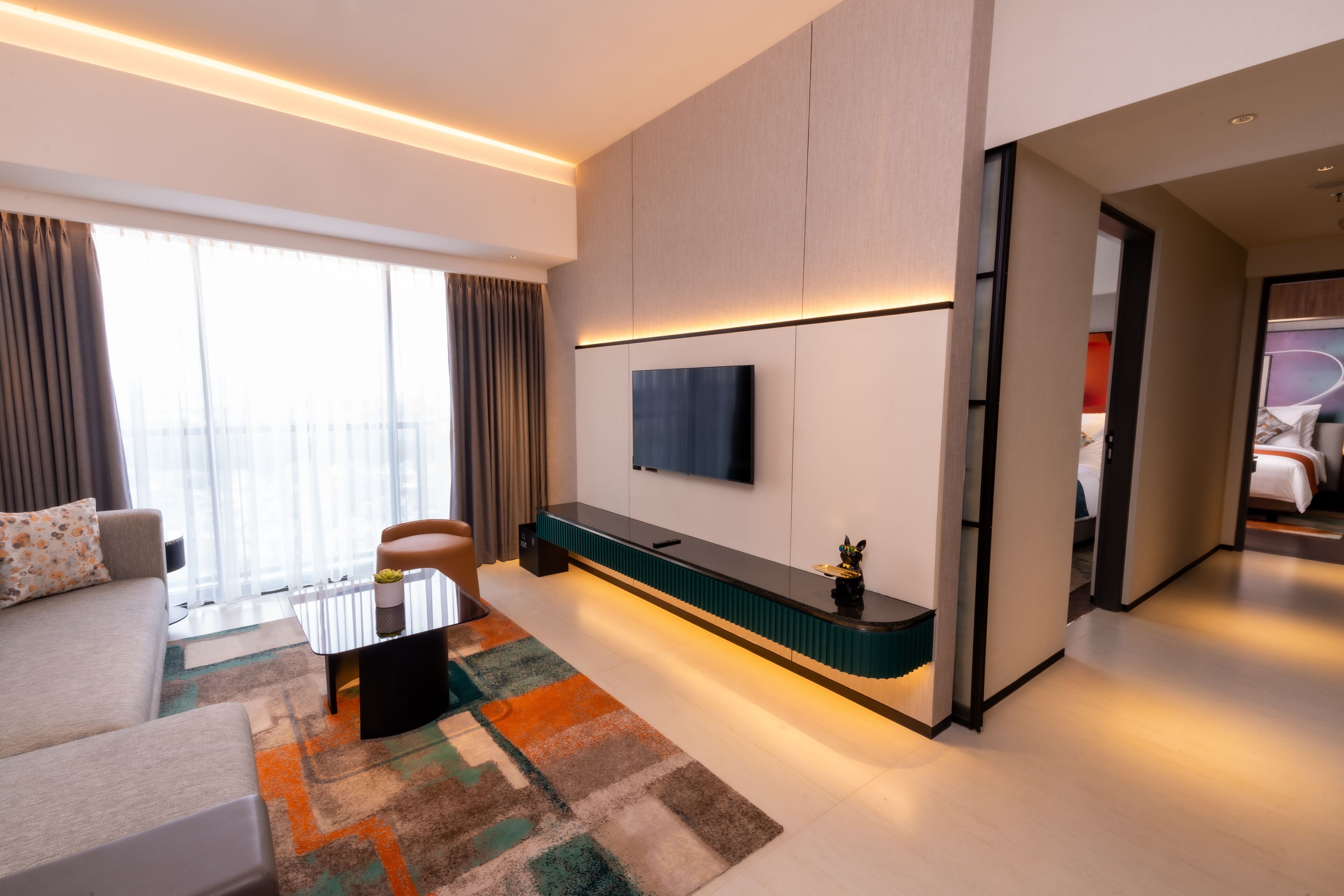 Una moderna camera d'hotel con divano, tavolino, TV a muro e vista sulla città attraverso ampie finestre.
