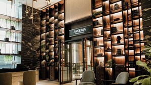 A modern interior with a reception desk, seating area, and a wall with shelves displaying books and decorative items. - Herloom BSD (Gading Serpong)