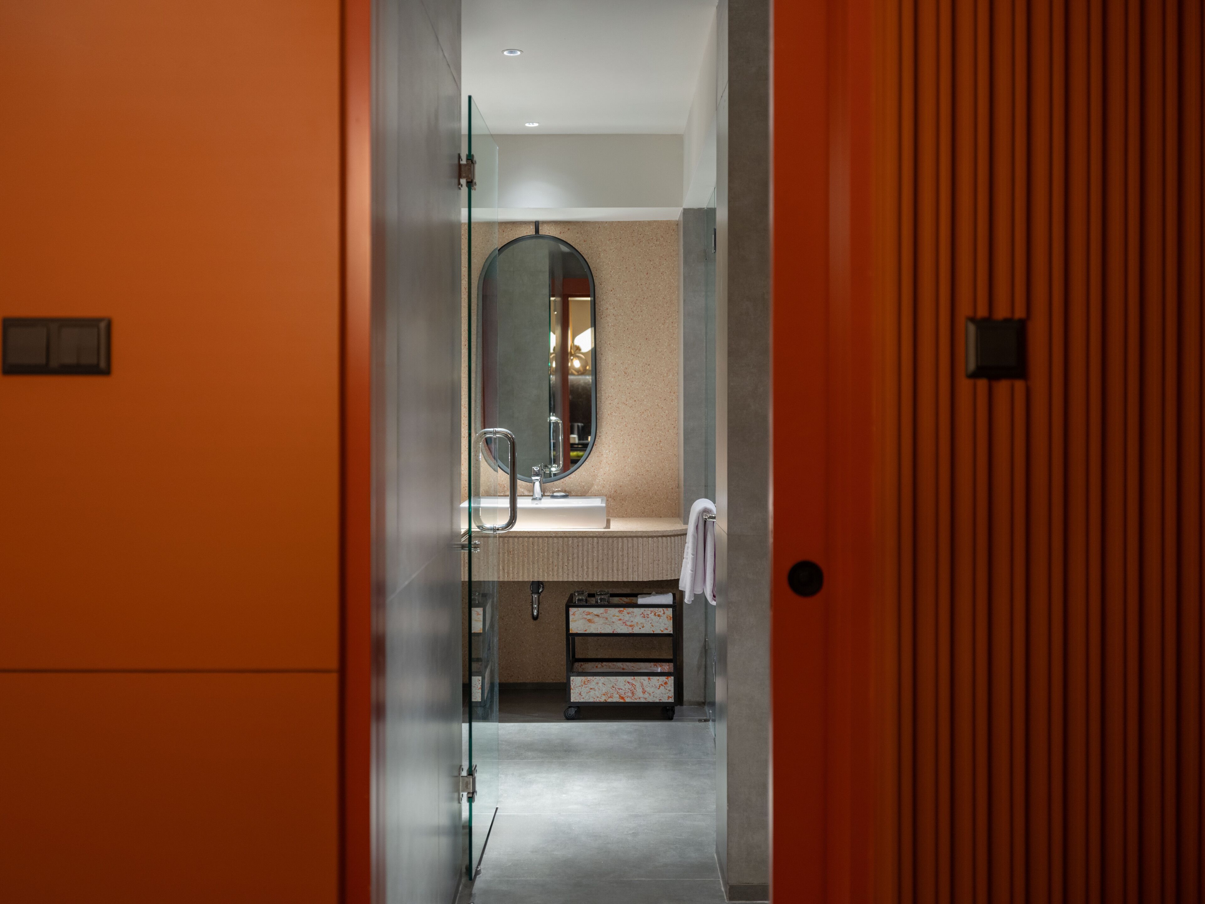 A modern bathroom with a glass partition, a round mirror, and a sink with a towel hanging on the wall.