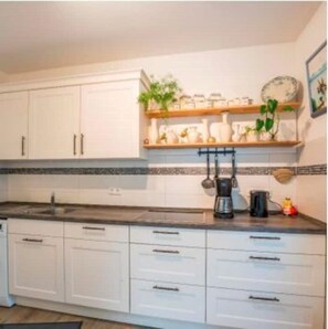 A kitchen with white cabinets, a black countertop, and a shelf with decorative items.