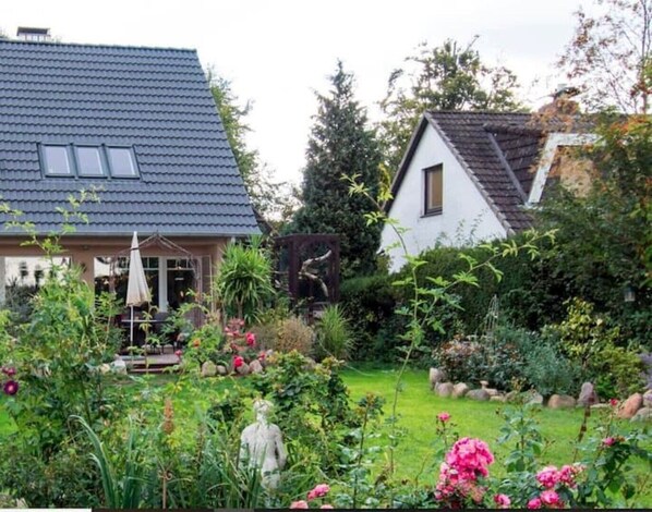 A residential garden with a house featuring a tiled roof and a white exterior.
