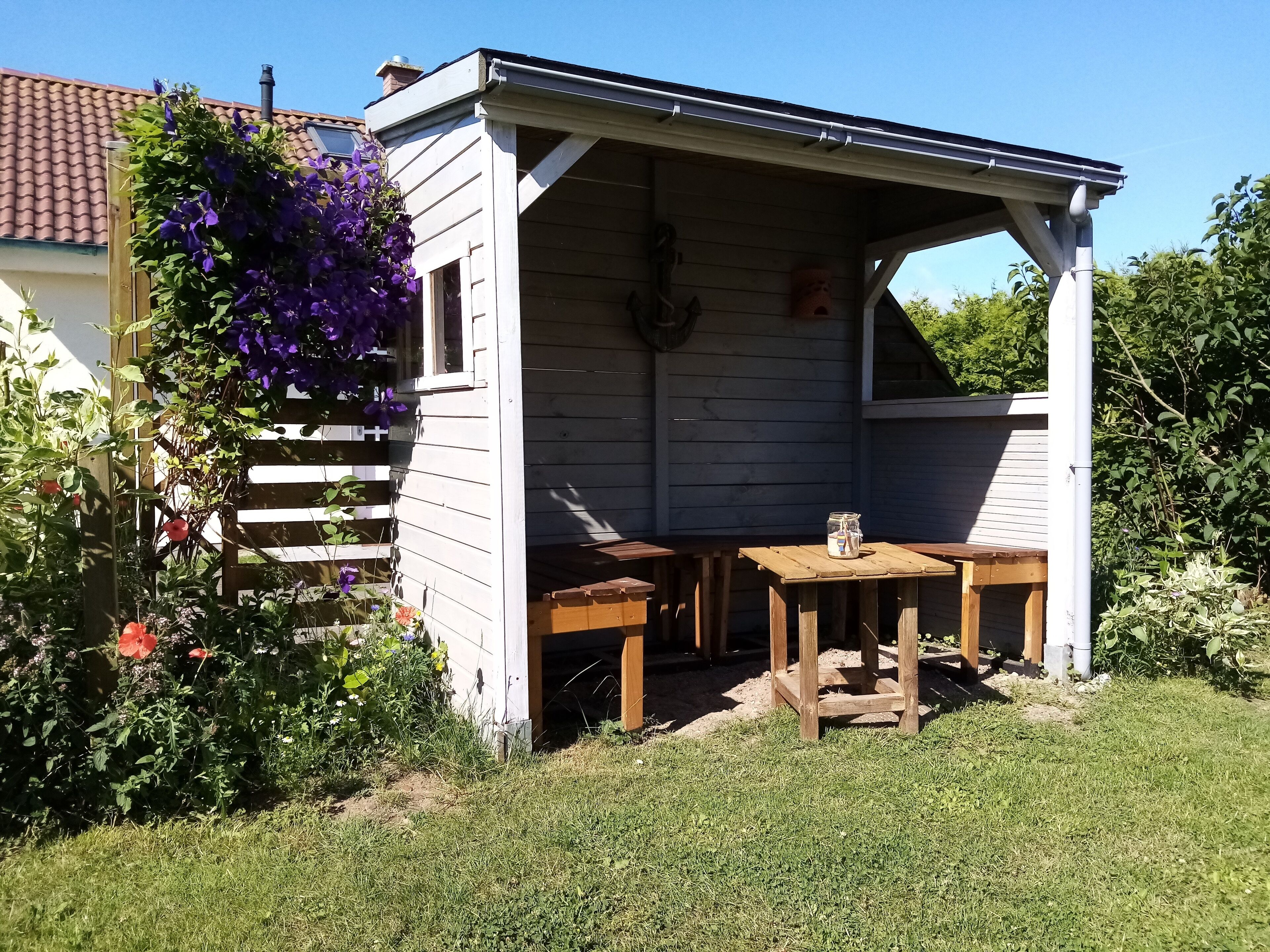 Una pequeña estructura de madera con un porche cubierto, una mesa de madera y una cesta colgante de flores.