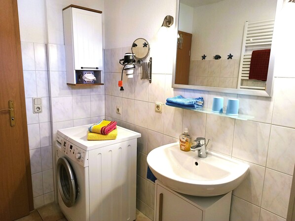 Une petite salle de bain équipée d’un lave-linge, d’un lavabo et d’un miroir.