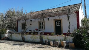 Uma casa rústica com telhado de telhas, porta da frente e um pequeno alpendre com mesa e cadeiras.