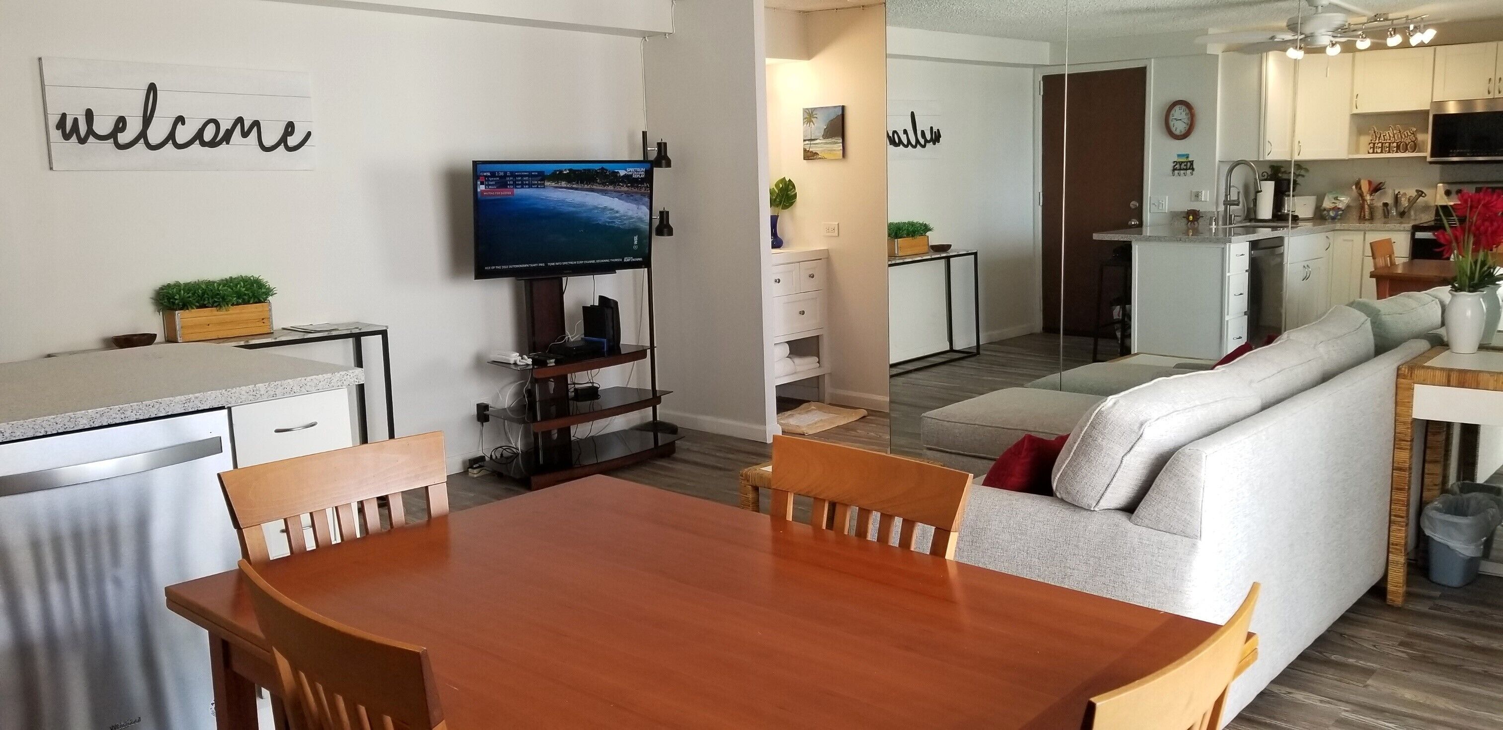 A modern living room with a wooden dining table, a sofa, and a TV mounted on the wall.