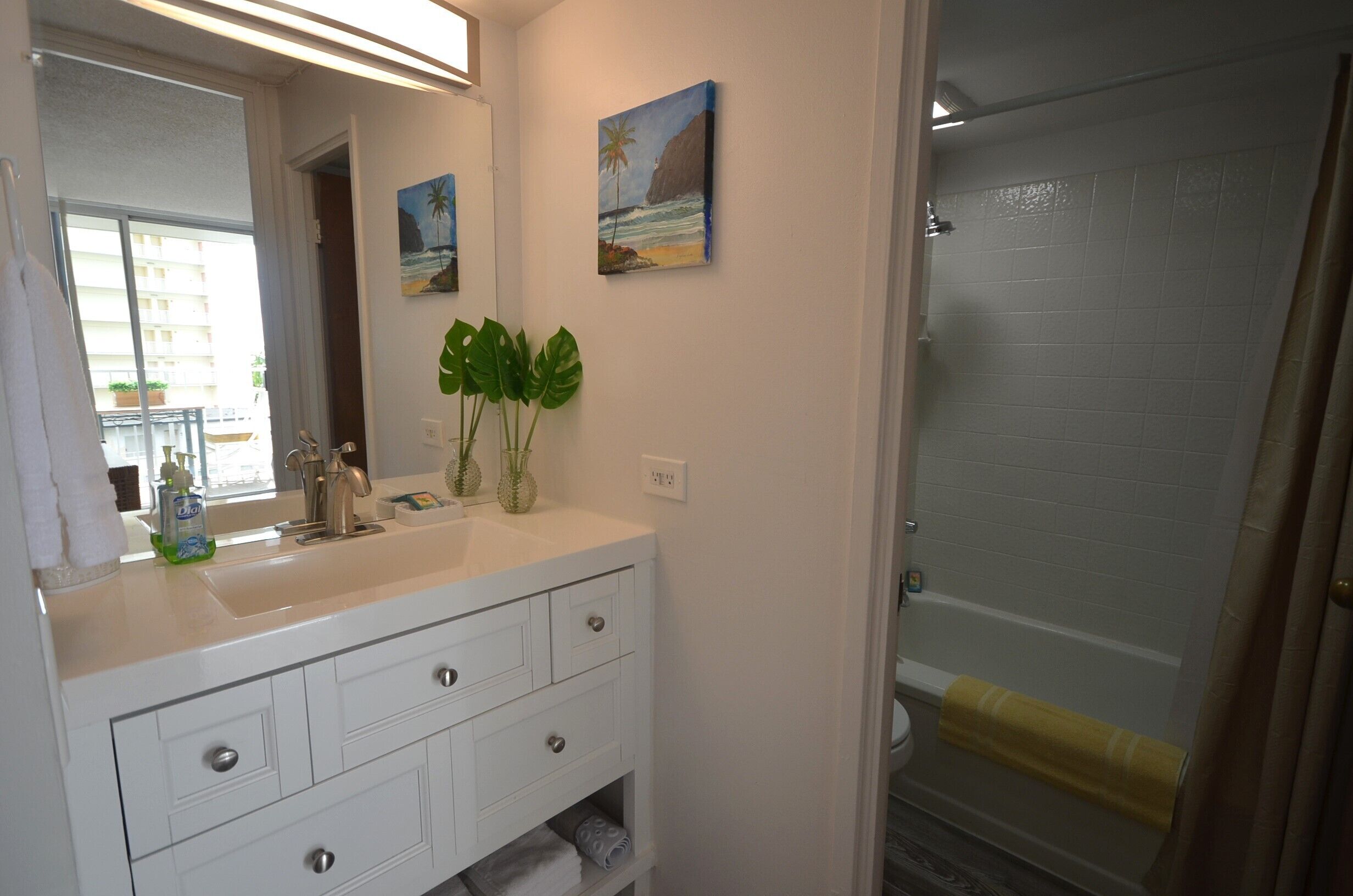 Une salle de bain avec un meuble-lavabo blanc, un grand miroir, deux tableaux accrochés au mur et un espace douche.