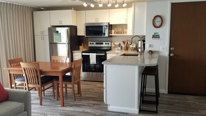 Une cuisine compacte comprenant un coin repas, un réfrigérateur, un four à micro-ondes, une cuisinière et une horloge murale.
