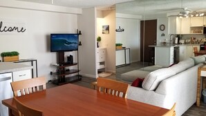 Un salon moderne avec une table à manger en bois, un canapé et un téléviseur diffusant une scène de surf.