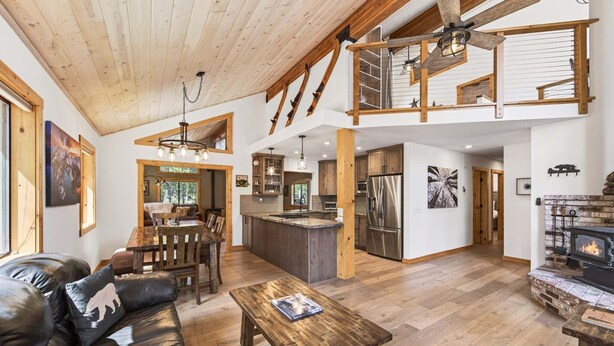 Amplia sala de estar con techo de madera, chimenea, comedor y cocina equipada con electrodomésticos modernos.