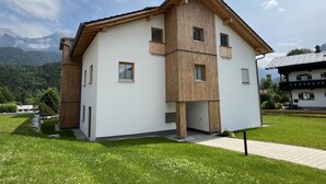 A two-story building with a white facade and wooden accents, set against a mountainous backdrop.