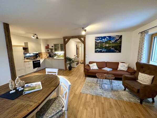 A modern living room with a brown sofa, a dining table with chairs, and a kitchen in the background.
