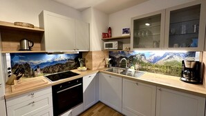 A modern kitchen with white cabinets, a stainless steel sink, and a microwave. There's a wooden countertop with a coffee maker and a knife block.