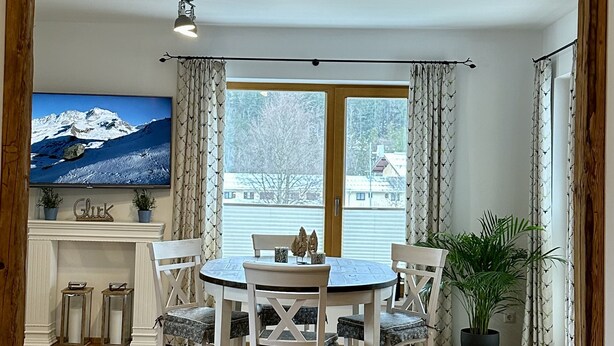 A dining area with a wooden ceiling, a television, and a view of a snowy landscape through large windows.