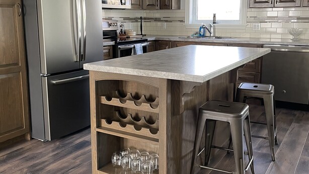 A modern kitchen with wooden cabinets, stainless steel appliances, a central island with wine glasses, and bar stools. - Countryside Getaway (Clyde River)