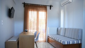 Una habitación pequeña con un sofá, una mesita de madera, una silla y un televisor montado en la pared.