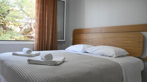 Una cama bien hecha con cabecera de madera, sábanas blancas y una toalla enrollada al lado.