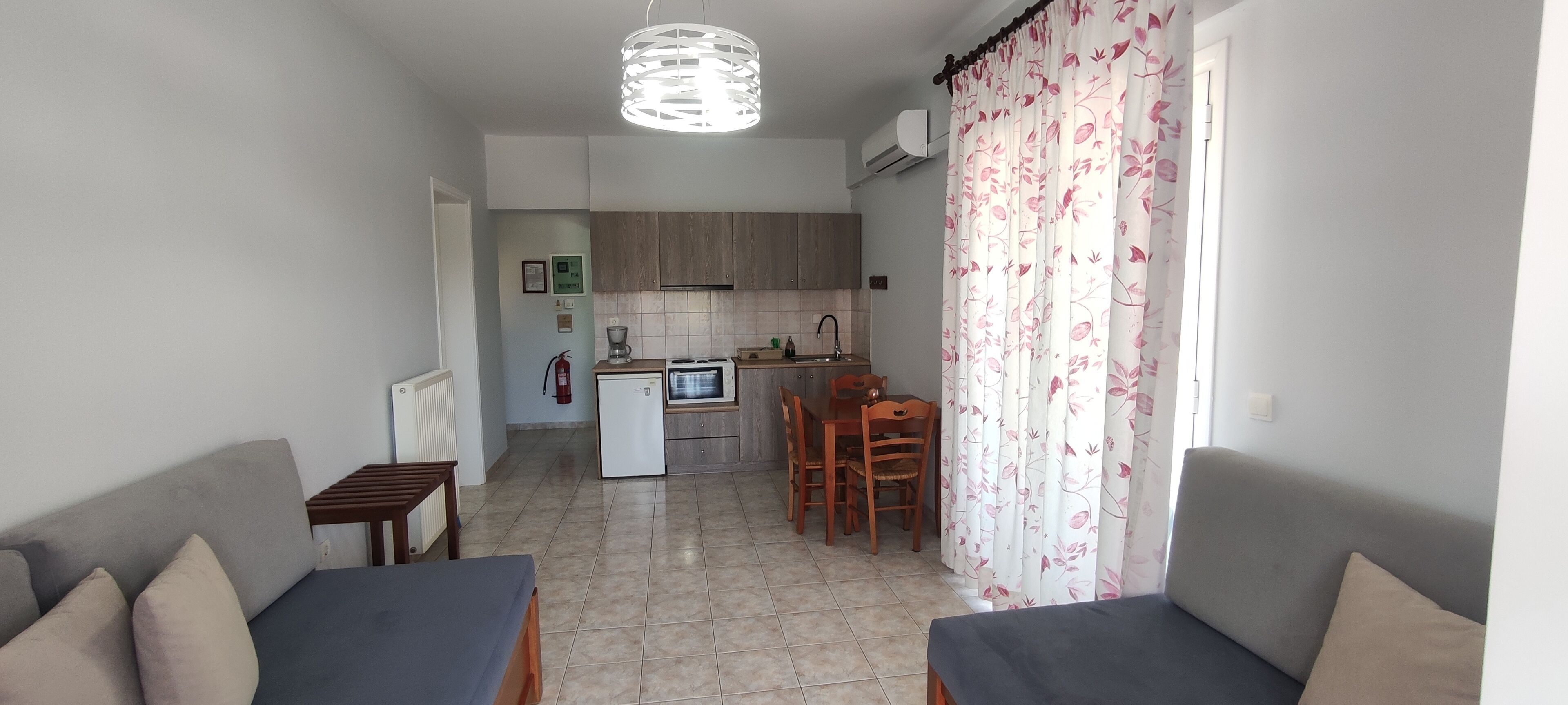 Un espacio habitable compacto con kitchenette, zona de comedor y área de estar con sofá y pequeña mesa.