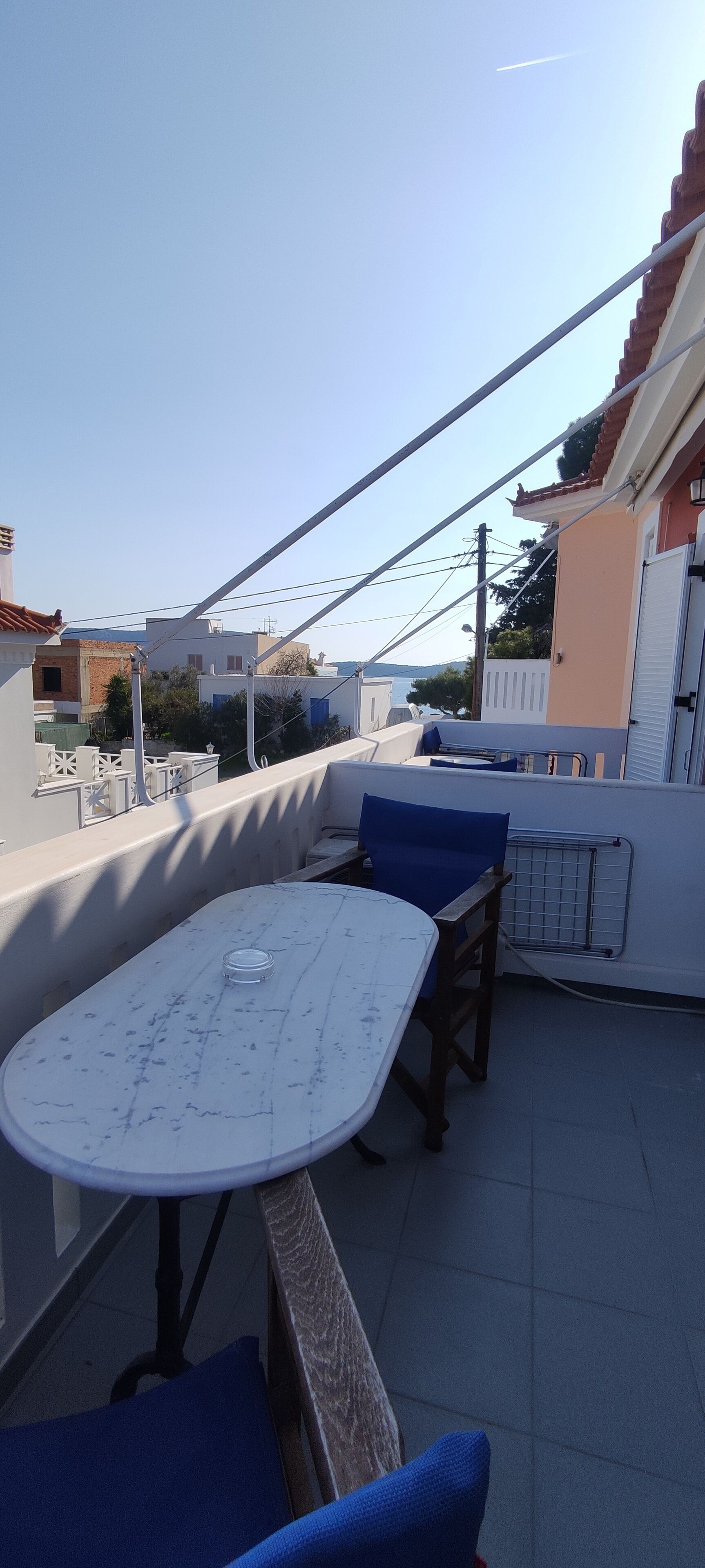 A rooftop terrace with a round table and blue chairs, surrounded by a white railing.