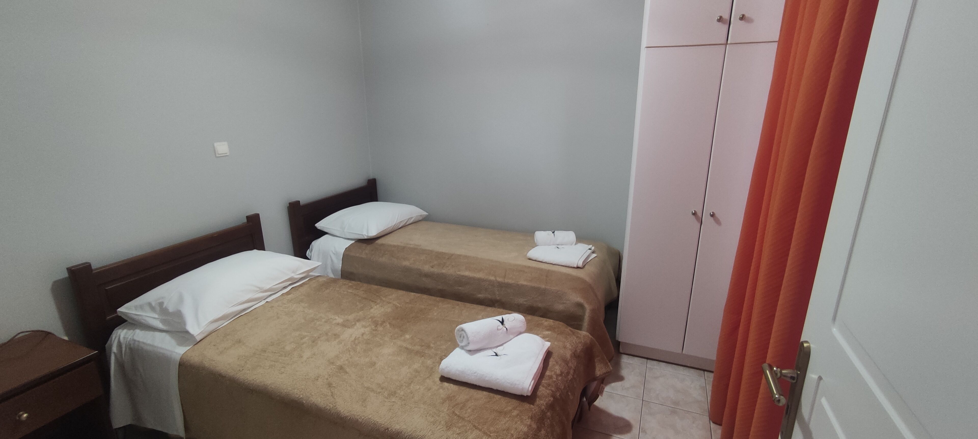 A small, clean room with two single beds, a wardrobe, and a nightstand.