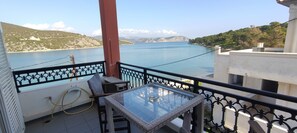 A balcony with a glass table and chairs, overlooking a calm sea and distant hills. - Vasilis Apartments (Ermionida)