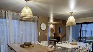 Una cocina moderna con una isla central, luces colgantes y un comedor con sillas blancas.