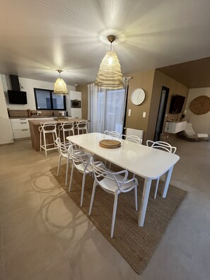 Una cocina moderna con armarios blancos, un comedor con mesa y sillas blancas, y una lámpara en el techo.