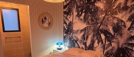 A bedroom with a bed, a nightstand, a wall-mounted TV, a patterned wall, and a hanging light fixture.