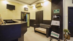 A reception area with a reception desk, a sofa, a TV mounted on the wall, and a sign indicating a surveillance area. - Hotel Mulberry (Kolkata)