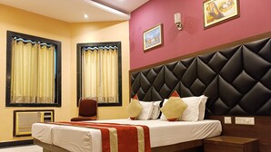 A hotel room with a large bed, a headboard, a bedside table, a chair, and a window with curtains. - Hotel Mulberry (Kolkata)