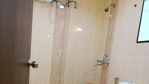 A bathroom with a toilet, shower, and a small green and red bucket. - Hotel Mulberry (Kolkata)