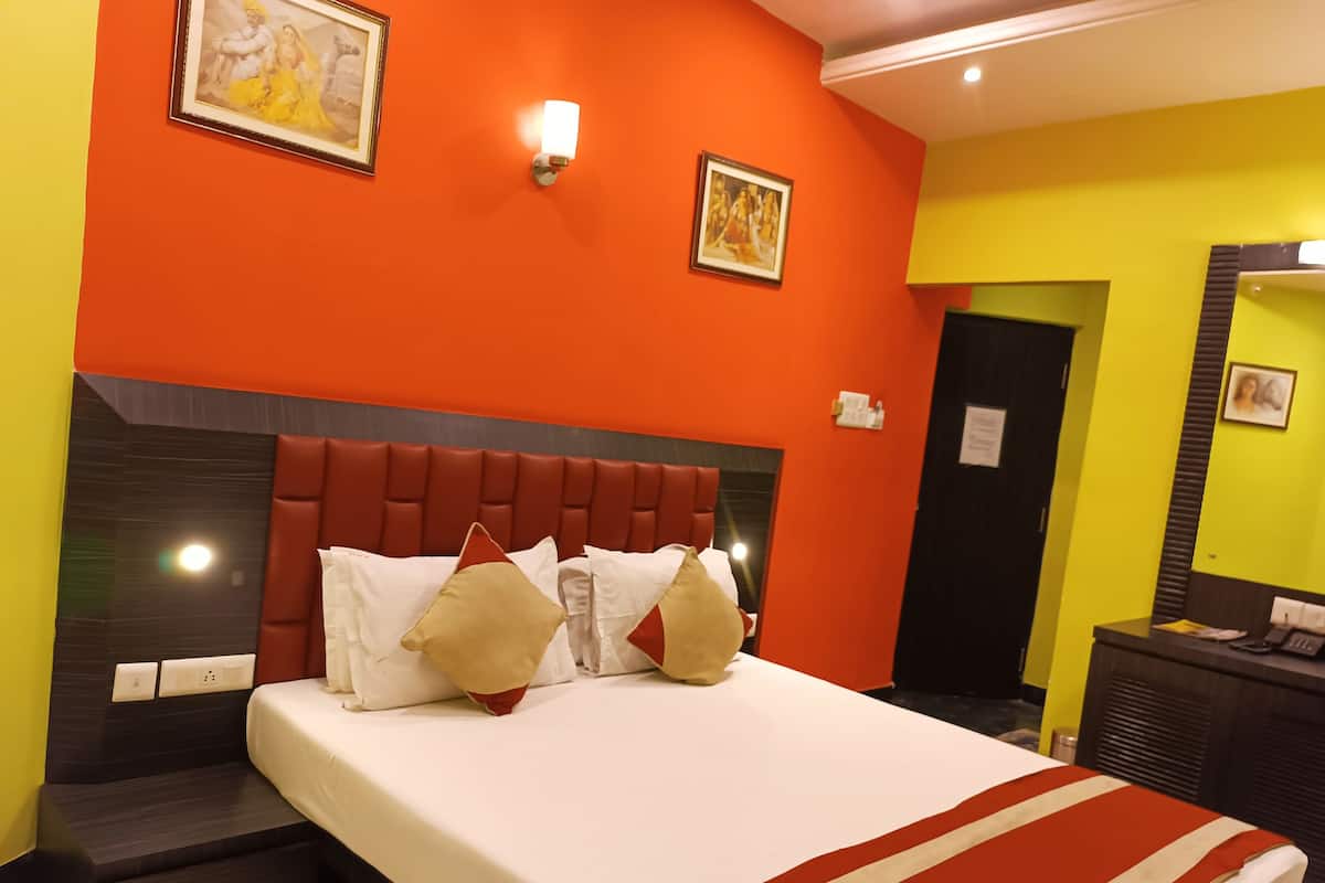 Ein Hotelzimmer mit einem großen Bett, orangefarbenen Wänden und einem roten Kopfteil. Zwei Wandleuchten und ein gerahmtes Bild sind über dem Bett angebracht.