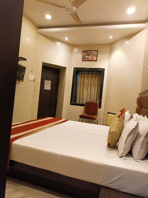 A hotel room with a bed, a chair, a window with curtains, a ceiling fan, and a wall-mounted painting. - Hotel Mulberry (Kolkata)