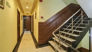 A hotel hallway with a wooden staircase and a carpeted floor. - Hotel Mulberry (Kolkata)