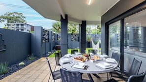 A modern outdoor dining area with a round table, black chairs, and a glass partition.