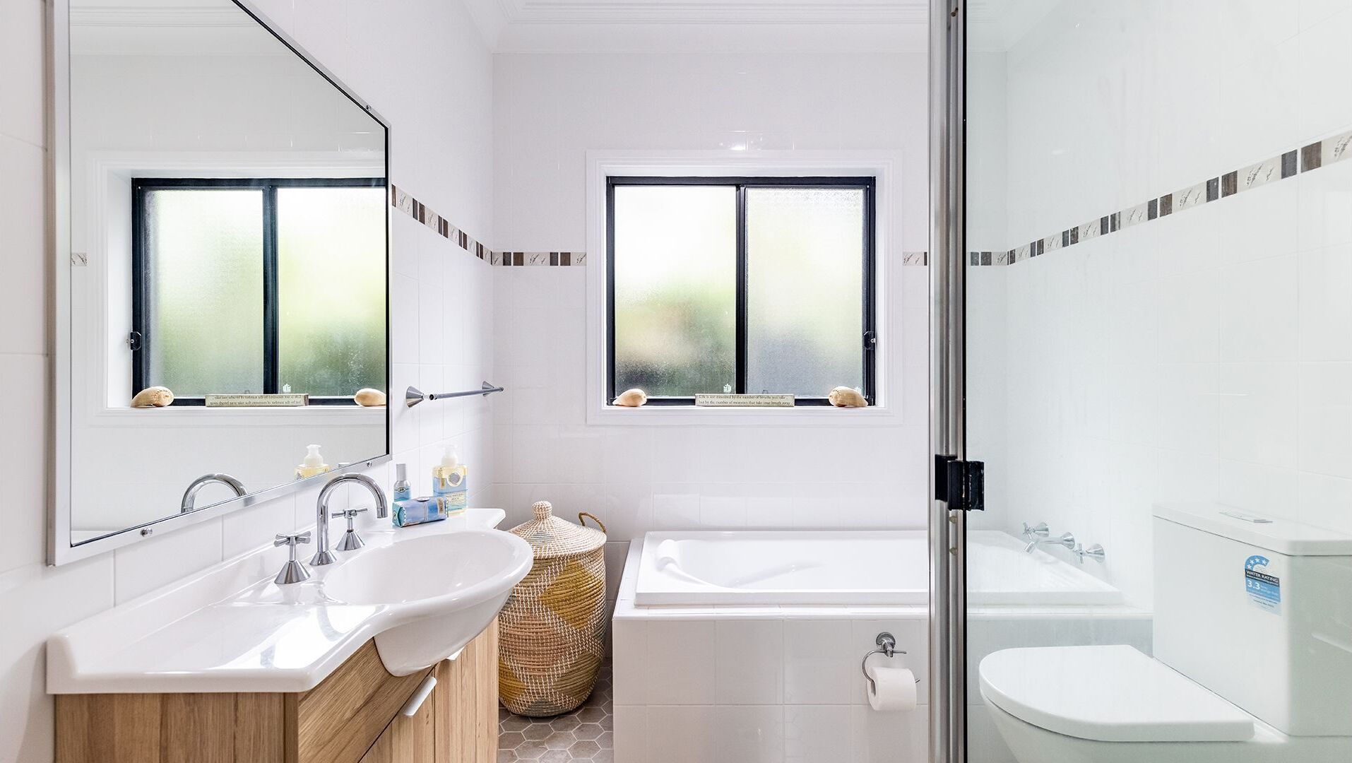 Une salle de bain moderne avec deux lavabos, une baignoire et des toilettes. Elle est dotée de fenêtres à vitres dépolies et offre une vue sur la verdure environnante.