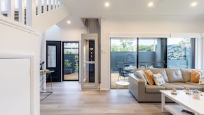 A modern living room with a sofa, coffee table, and a dining area with a table and chairs. - Beach Haven, 3a Messines Street - 4 Minute walk to the beach, WiFi , Air Con (Shoal Bay)