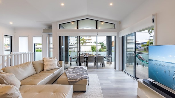 A modern living room with a sofa, a dining area, and a large TV screen. - Beach Haven, 3a Messines Street - 4 Minute walk to the beach, WiFi , Air Con (Shoal Bay)