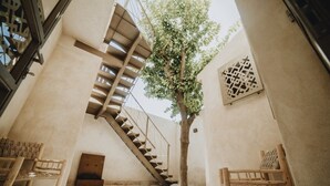 Un estrecho pasillo interior con una escalera de madera, un árbol y dos sillas de madera.