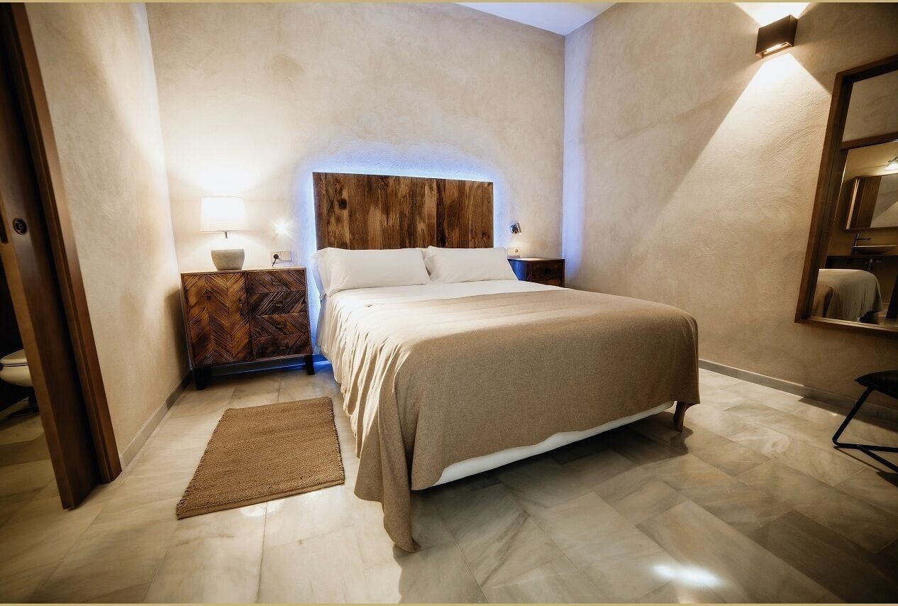 A bedroom with a bed, a nightstand, a lamp, a mirror, and a wooden headboard.