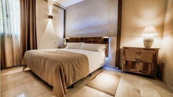 Un dormitorio ordenado con una cama grande, una mesita de noche de madera con una lámpara y un armario pequeño de madera.