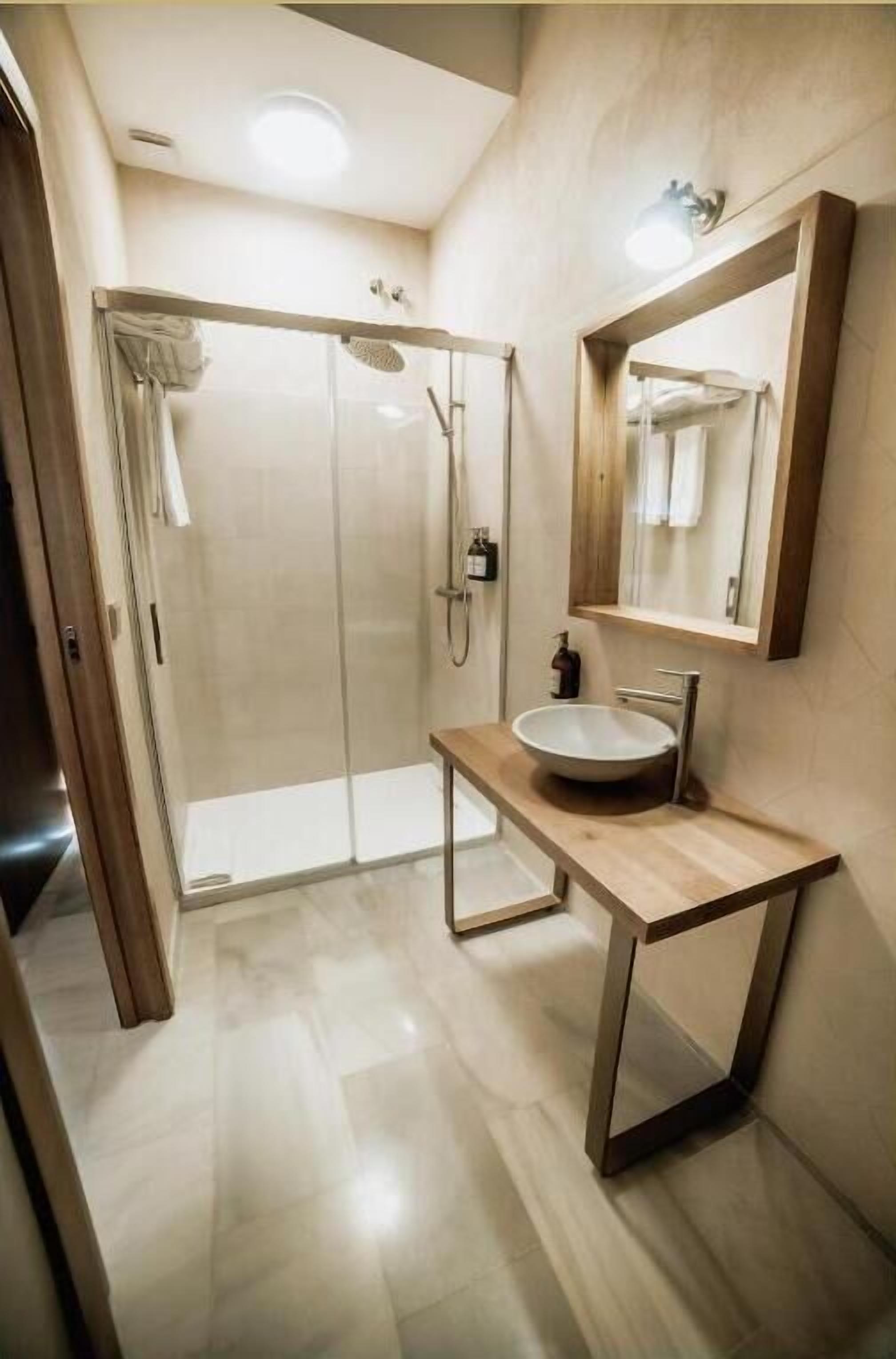Un baño moderno con cabina de ducha de vidrio, tocador de madera con lavamanos y espejo.