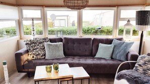 Een moderne woonkamer met een hoekbank, een salontafel en uitzicht op een huis door grote ramen.