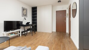 A modern living room with a flat-screen TV, a desk, and a bookshelf.