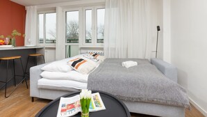 A modern bedroom with a bed, a small desk, and a window with curtains.