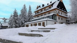 Ein mehrstöckiges Gebäude mit schneebedecktem Dach und umliegenden Bäumen.